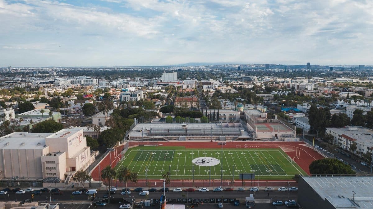 Drone shot capturing an urban football stadium and surrounding cityscape under a bright sky.