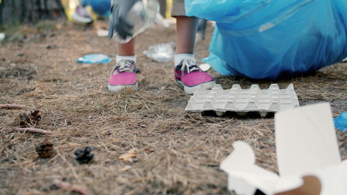 People cleaning up litter in a pine forest with focus on feet and garbage.