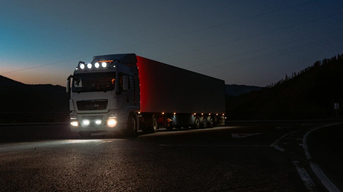 A heavy-duty truck navigates a quiet road at dusk, highlighting its illuminated path through remote mountains.