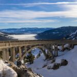 Breathtaking winter view of Donner Summit Bridge amidst snow-covered mountains and blue skies.