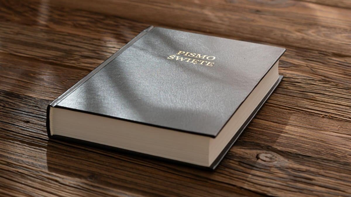 A close-up of a Polish Bible on a wooden table, under warm sunlight.