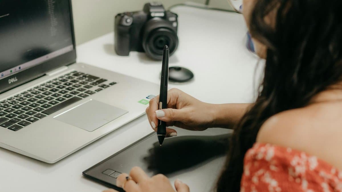 A woman using a digital tablet and stylus next to a laptop, showcasing modern design technology.