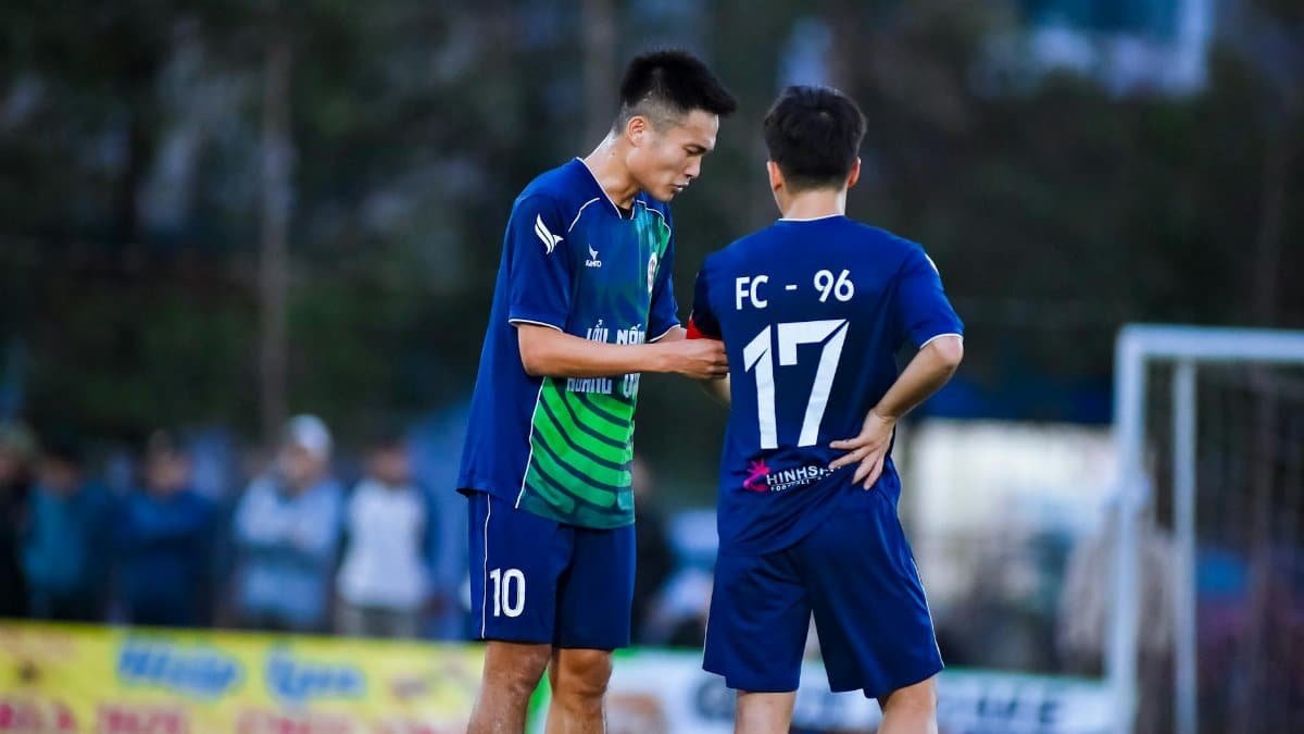 Two soccer players in blue jerseys strategize during a match in Hà Nội, Vietnam.