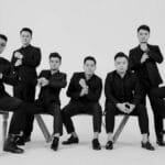 Stylish black and white portrait of seven men posing in suits, demonstrating elegance and fashion.