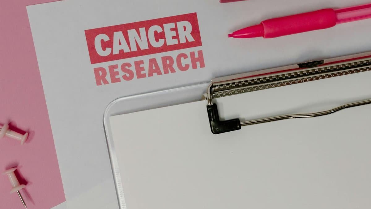 Flat lay of a cancer research paper on a clipboard with pink stationery items.