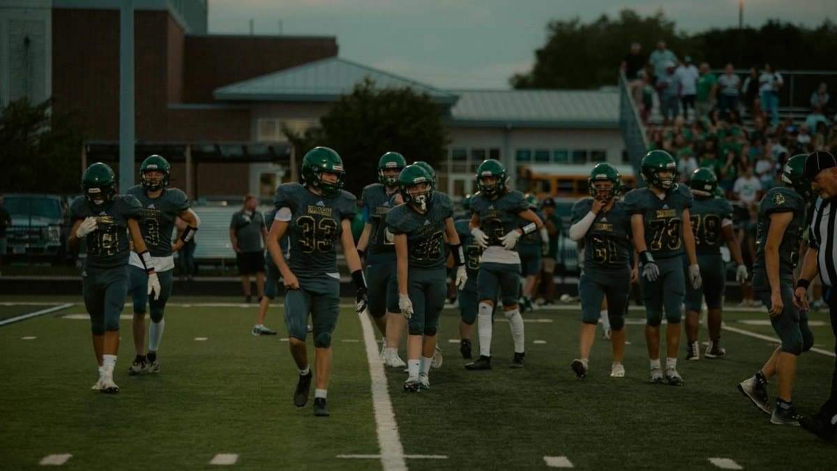 High school football players on the field preparing for a game in the evening.