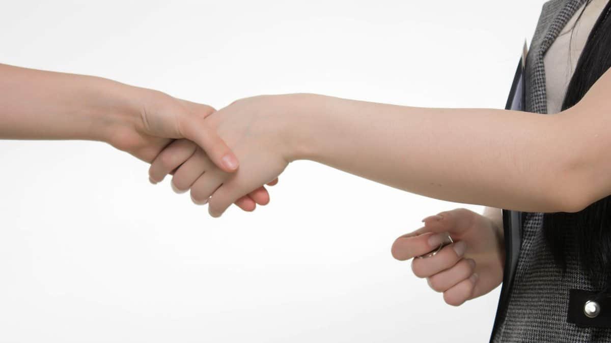 An up-close image of two people shaking hands in a professional setting against a white background.