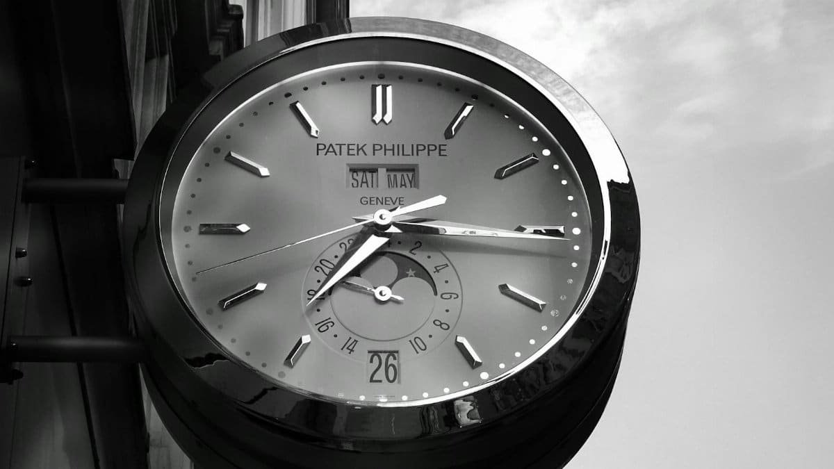 A close-up of a Patek Philippe wall clock with reflective surface showing time.