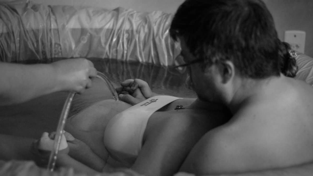 Black and white image of a couple during a home water birth, showcasing intimacy and support.