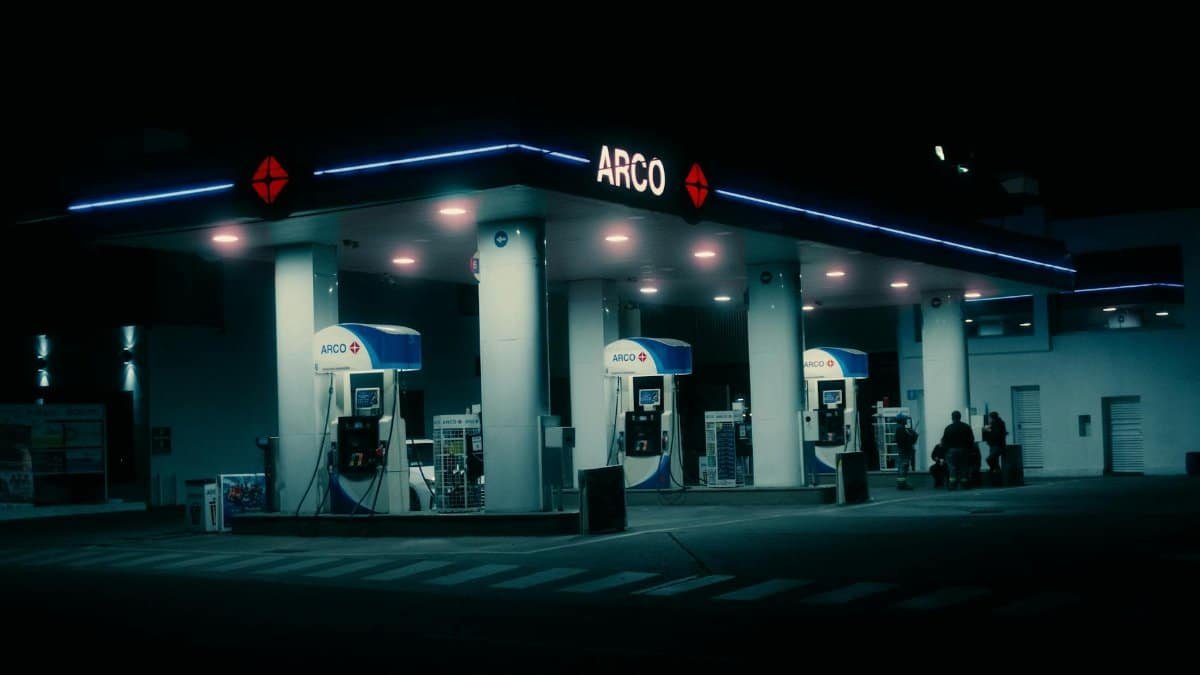 A cinematic night view of a modern ARCO gas station lit in neon against a dark backdrop.