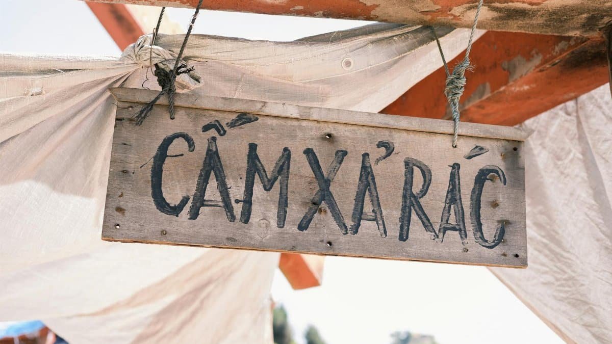 Hanging wooden sign with Vietnamese text outdoors, conveying a rustic and worn appearance.