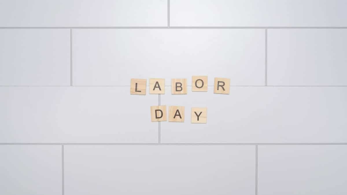 Wooden letter tiles spelling 'Labor Day' on a white tiled wall. Minimalist style.