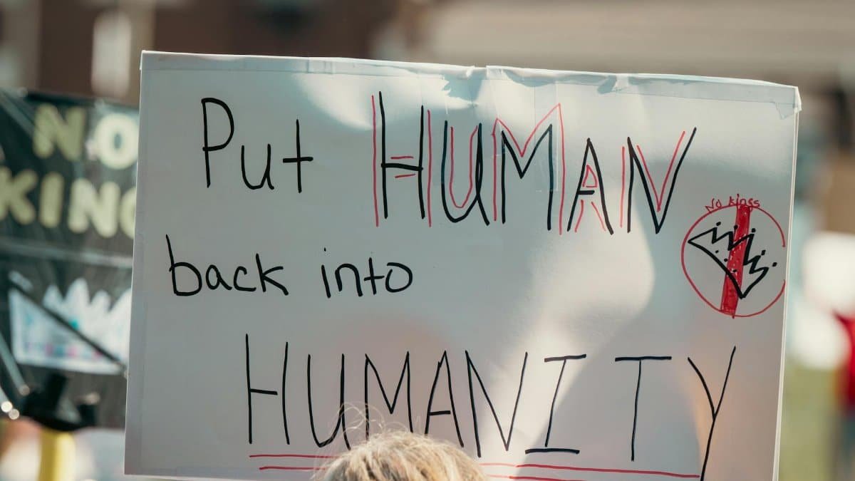 A protest sign with the message 'Put Human back into Humanity' during a daylight rally.