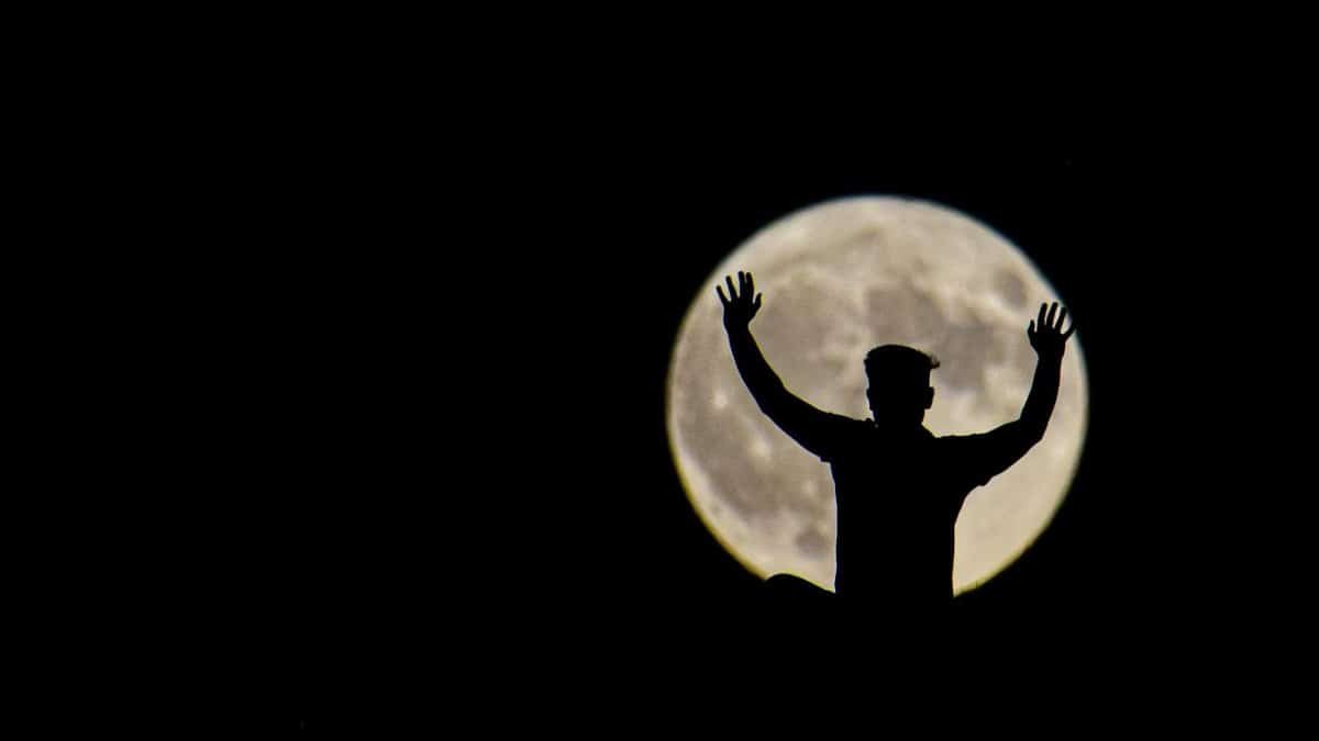 Captivating silhouette of a person with raised hands in front of a full moon.