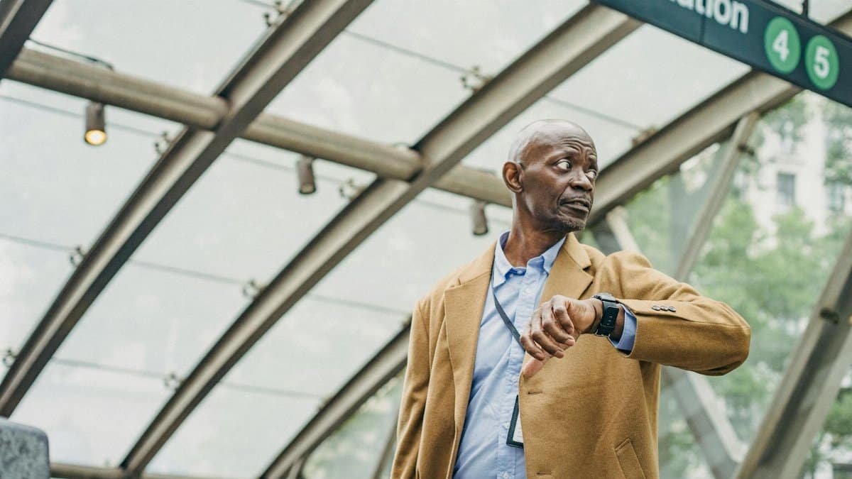 Serious African American businessman in formal clothes standing in subway station and checking time on wristwatch while looking away thoughtfully
