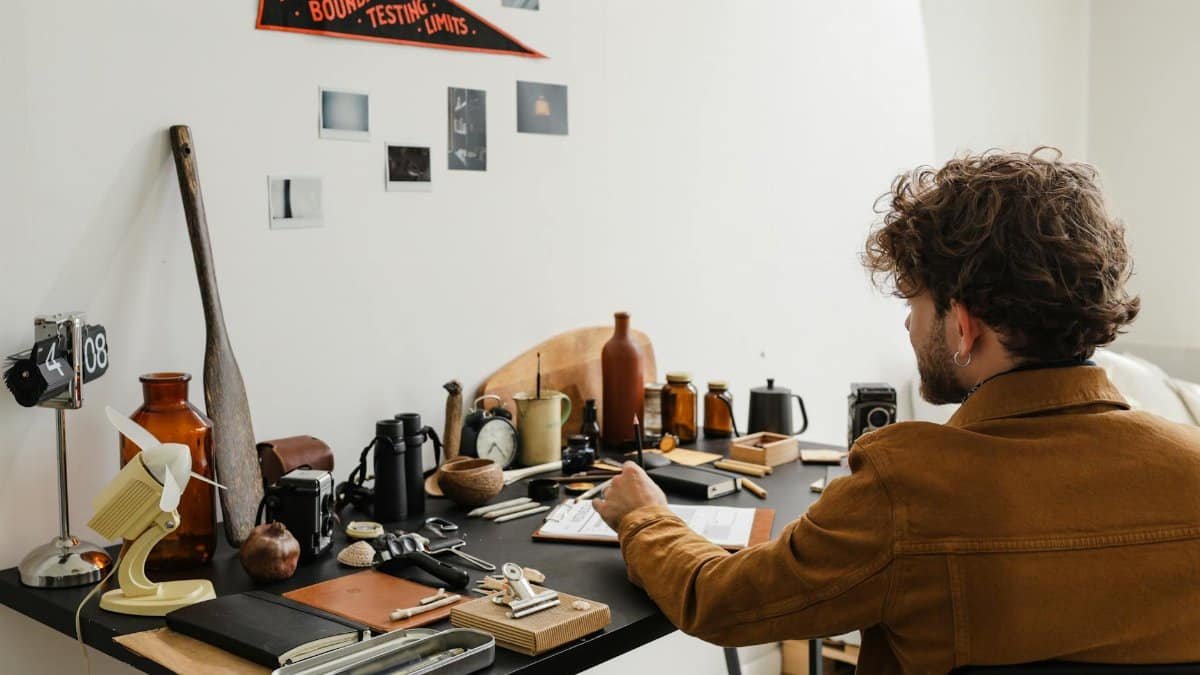 Man with wavy hair working at a creative desk, surrounded by vintage decor and tools.