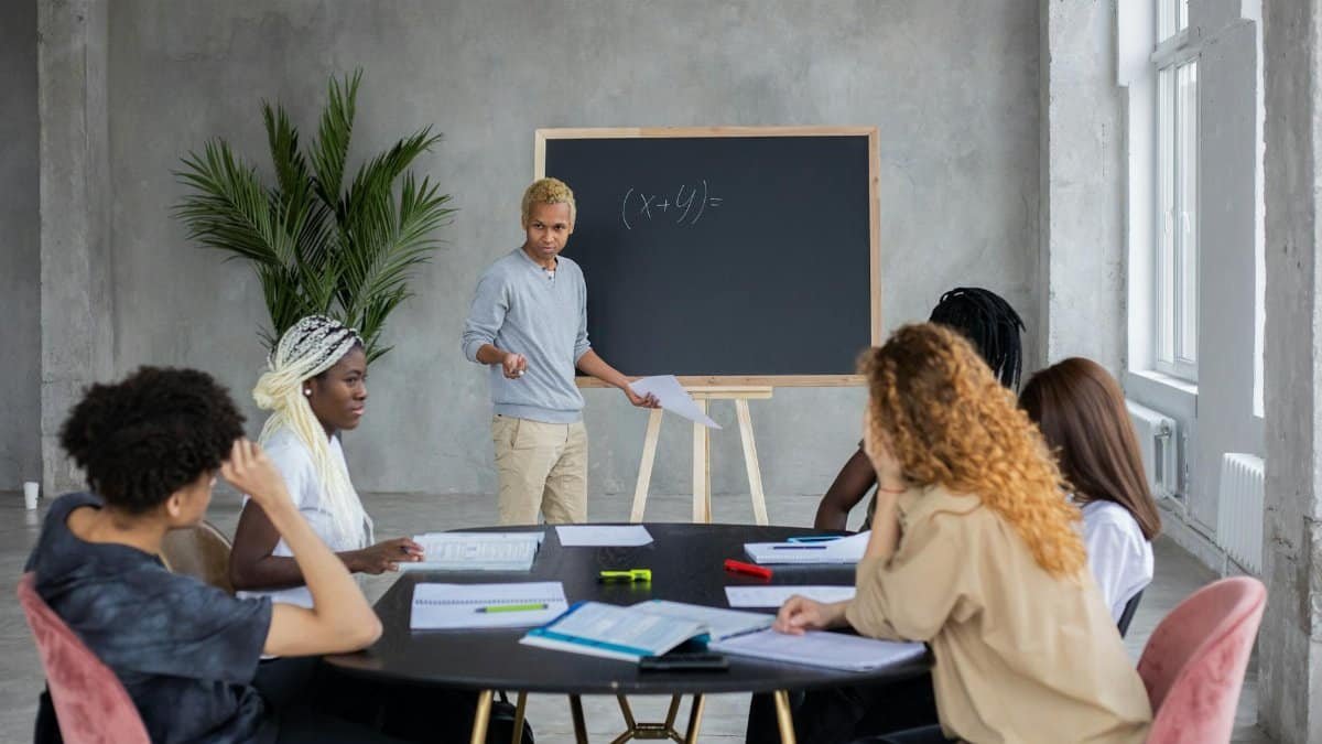 African American student explaining mathematic equation to diverse classmates while doing homework together in spacious room