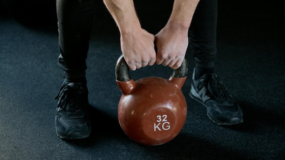 A person lifting a 32 kg kettlebell in a gym setting, showcasing strength training.
