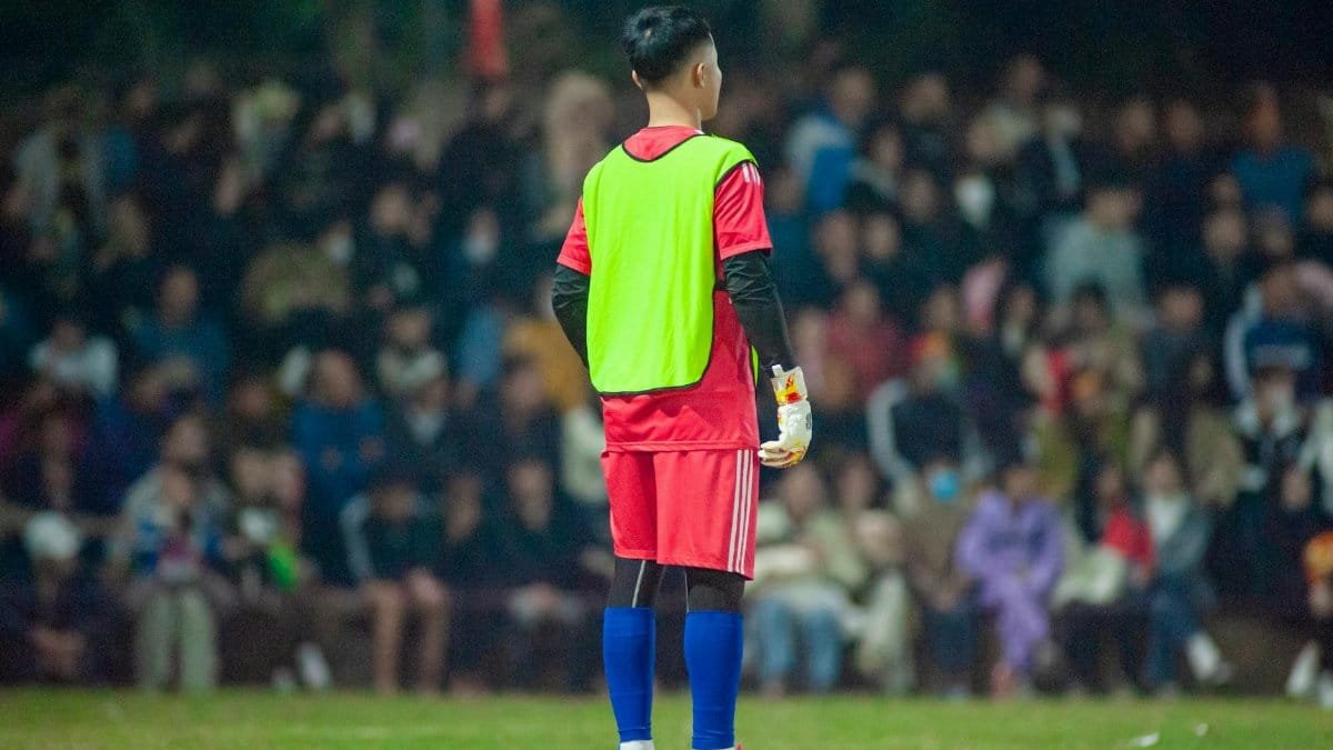 Soccer player in bright gear on the field at night in Hanoi, Vietnam faced towards the crowd.