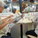 Two elderly men read newspapers inside a cafe in Bangkok, capturing a moment of daily life.