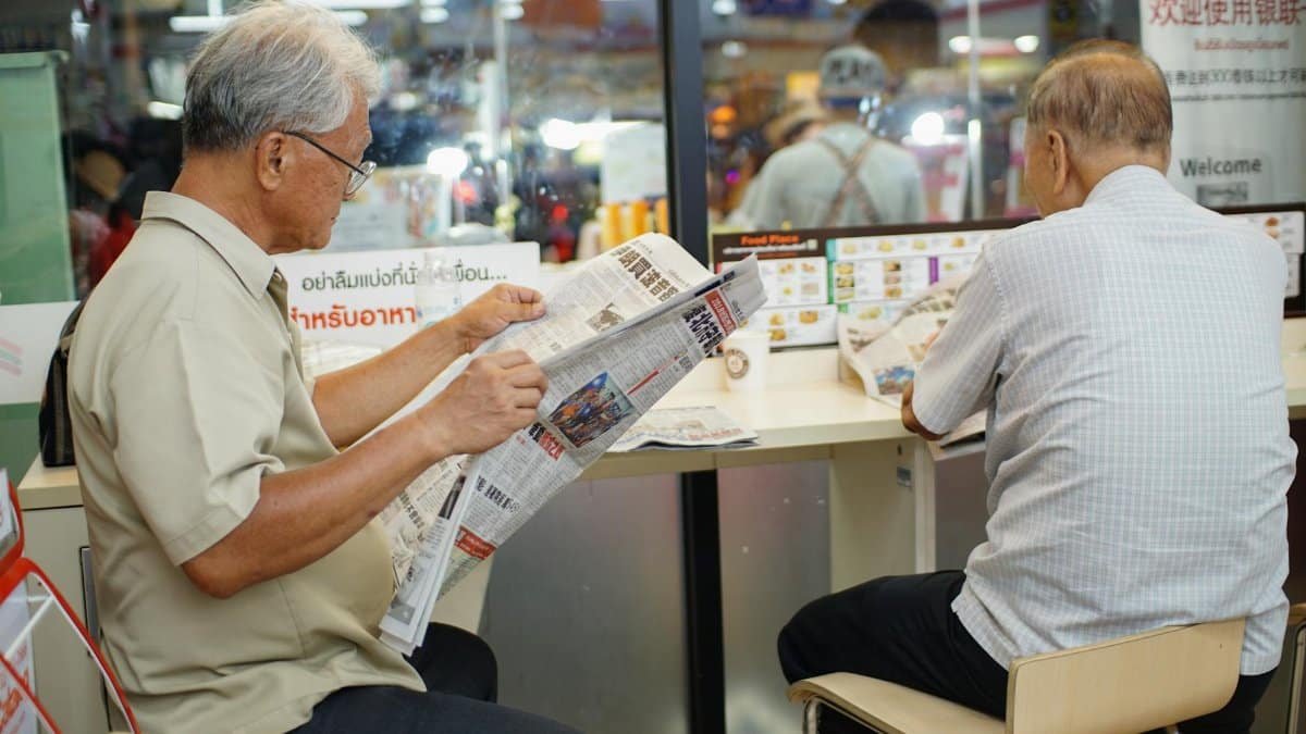 Two elderly men read newspapers inside a cafe in Bangkok, capturing a moment of daily life.