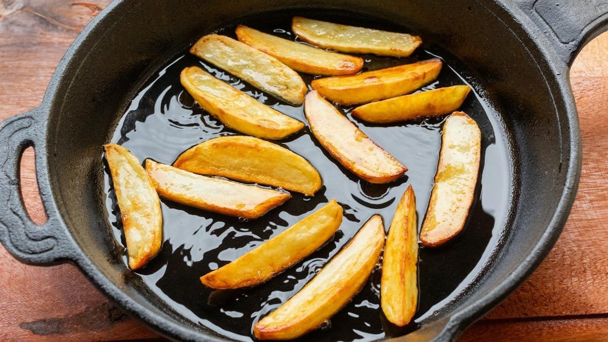 Freshly fried golden potato wedges sizzling in a cast iron skillet, showcasing delicious homemade cooking.