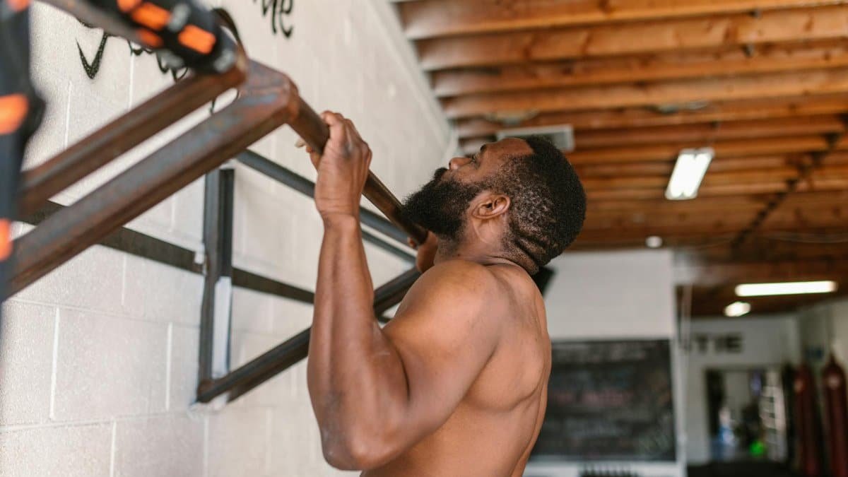 A shirtless man doing a pull-up exercise on a pull-up bar.