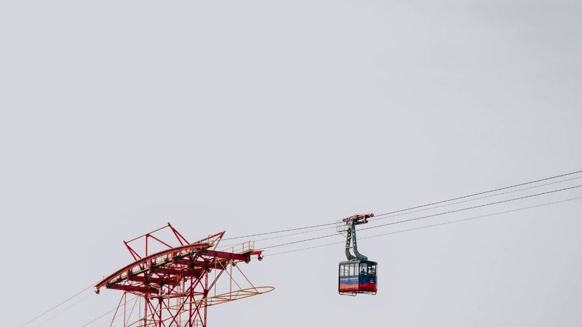 A red cable car gliding on steel cables against a minimalistic white sky. Perfect for travel or transportation themes.