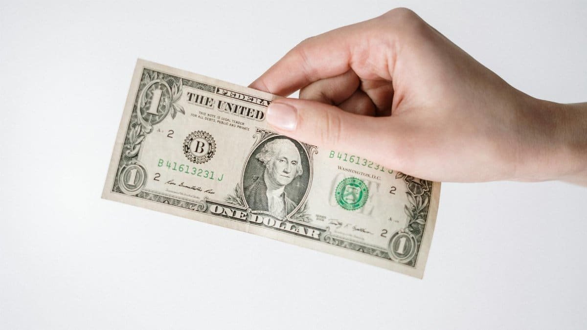 Close-up of a Caucasian hand holding a US one dollar bill against a white background.