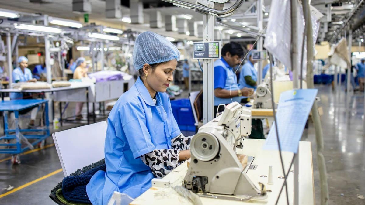 Workers in a textile factory operating sewing machines, wearing blue uniforms and hairnets, focused on their tasks.