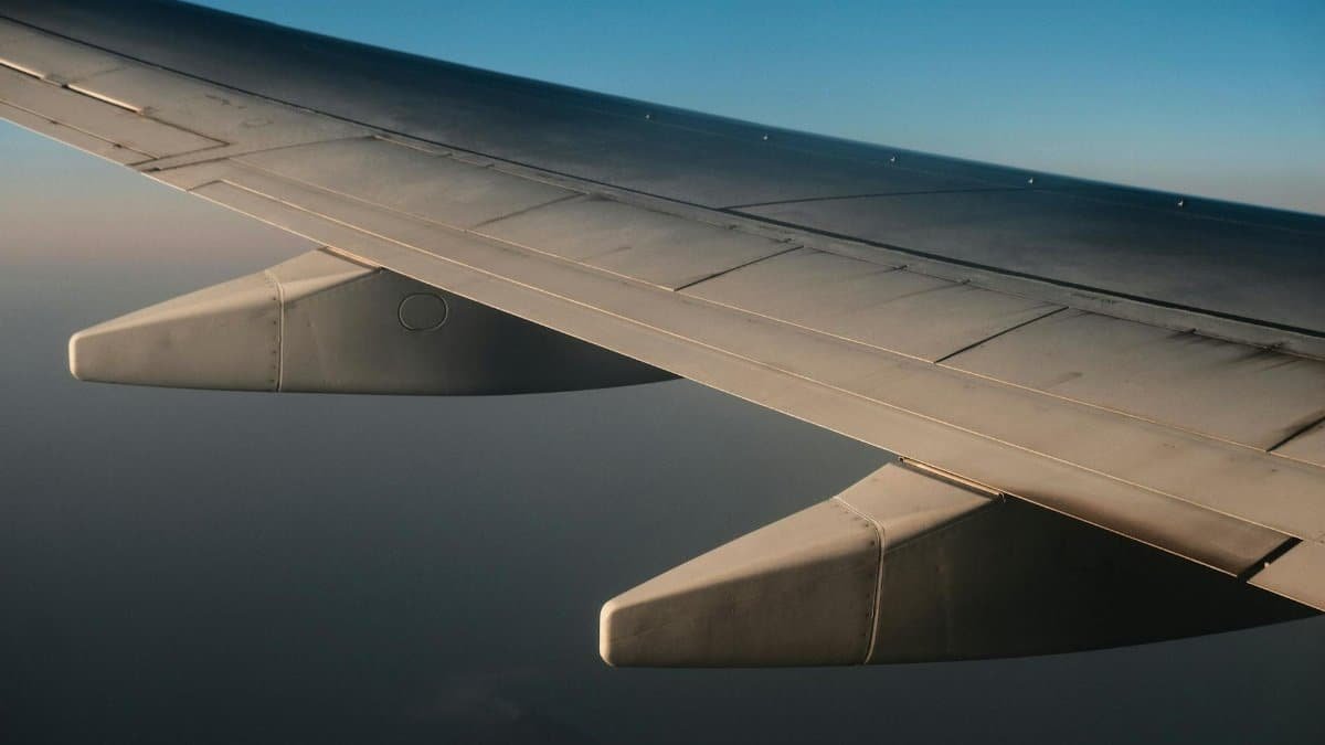 View of an airplane wing during flight with clear blue skies and serene clouds below.