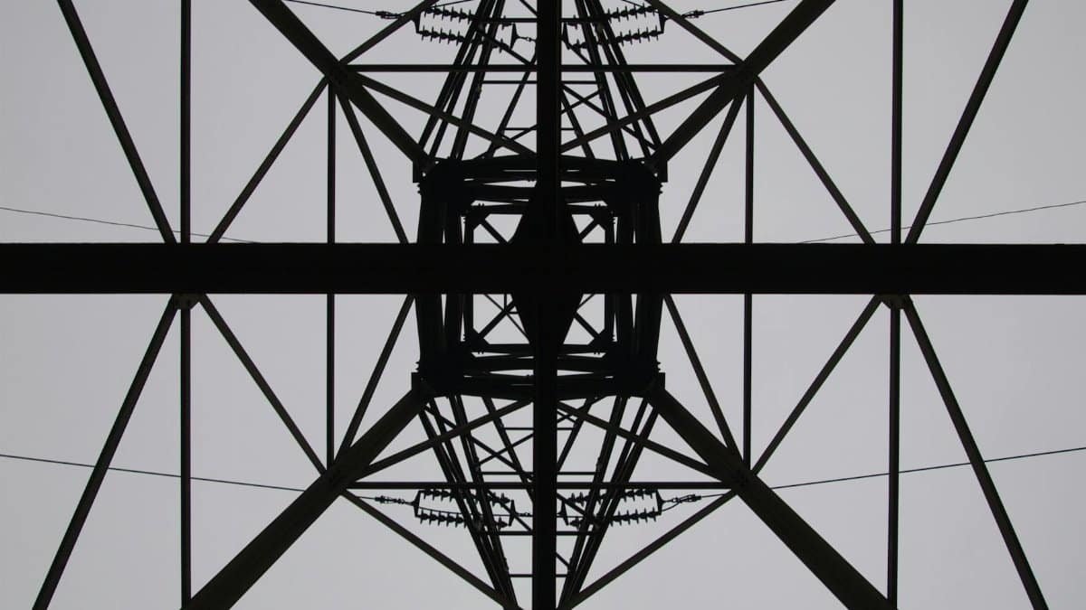 Abstract perspective of a steel power tower against the sky, showcasing intricate lattice design.