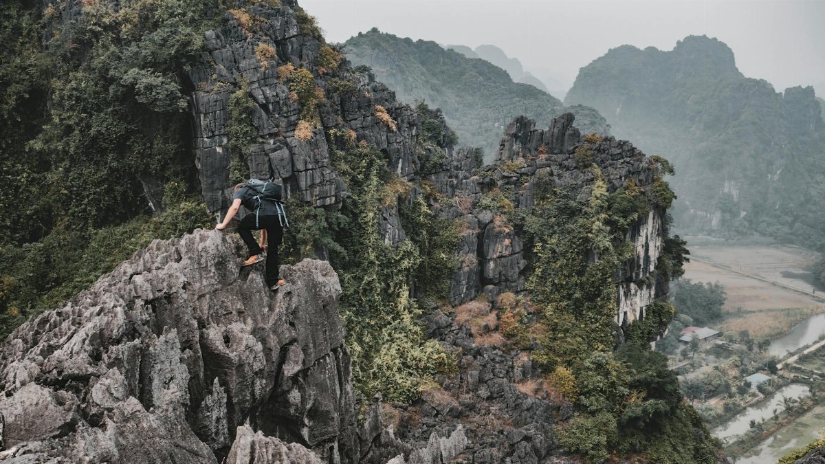 A hiker scales rugged limestone karsts in Hoa Lư, Vietnam, showcasing breathtaking natural beauty.