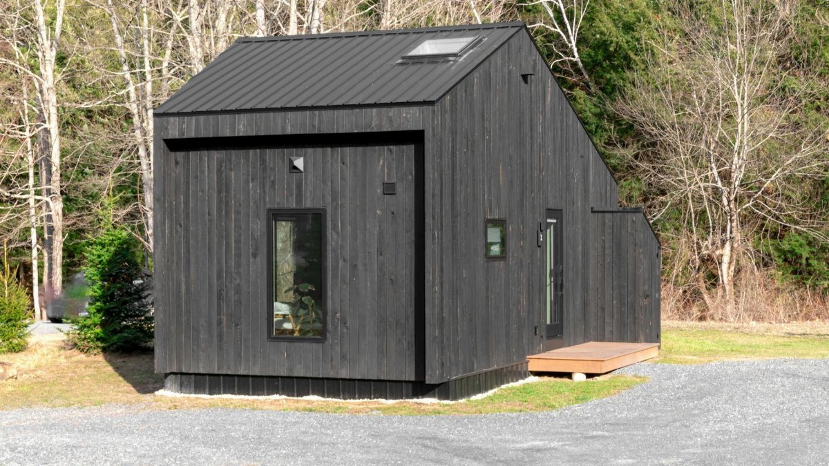 A minimalistic black tiny house nestled in a forest area, showcasing sustainable living.