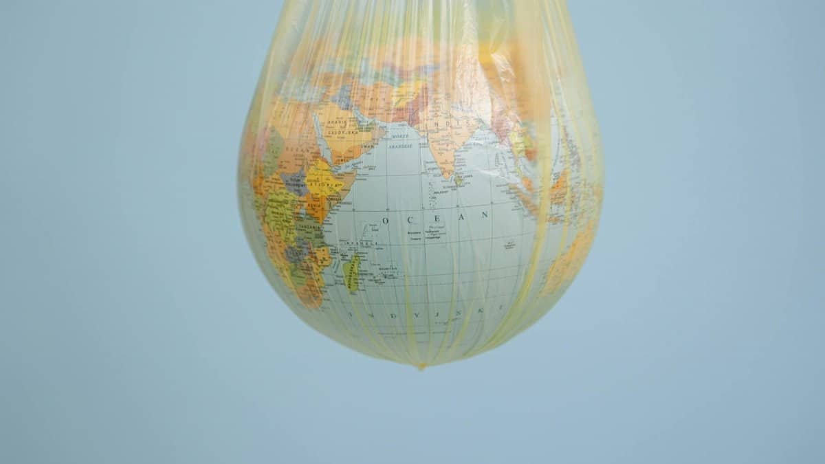 A globe wrapped in a plastic bag illustrating environmental concerns with a blue backdrop.