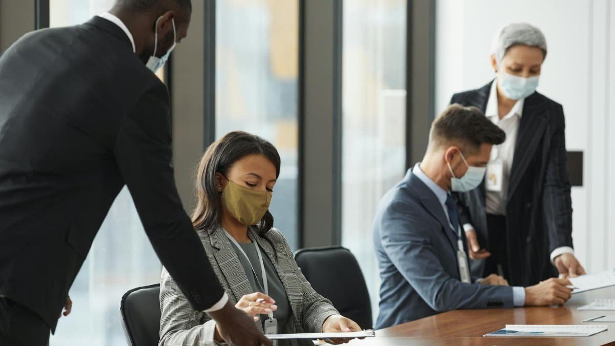 Business professionals wearing face masks in a meeting room, maintaining safety protocols.