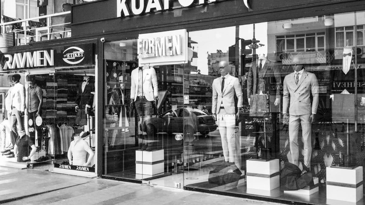 Black and white image of a men's fashion storefront showcasing elegant suits with mannequins prominently featured.