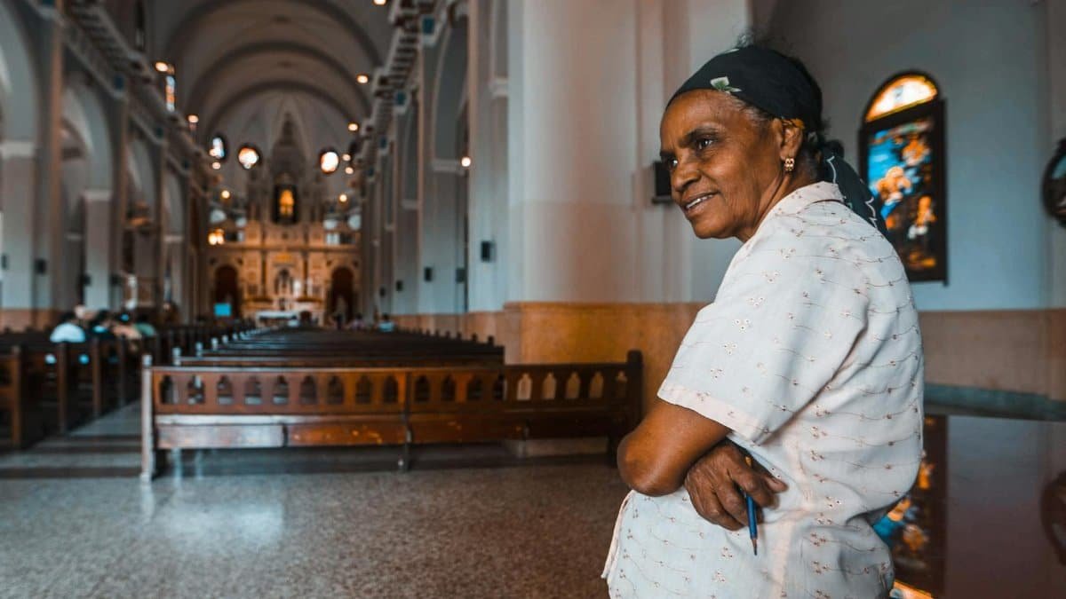 A senior woman standing in a beautifully arched church interior, exuding peace.
