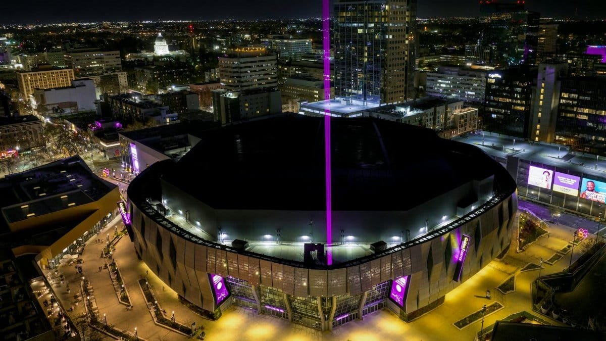 Aerial view of Golden 1 Center in downtown Sacramento illuminated at night with vibrant purple lights.