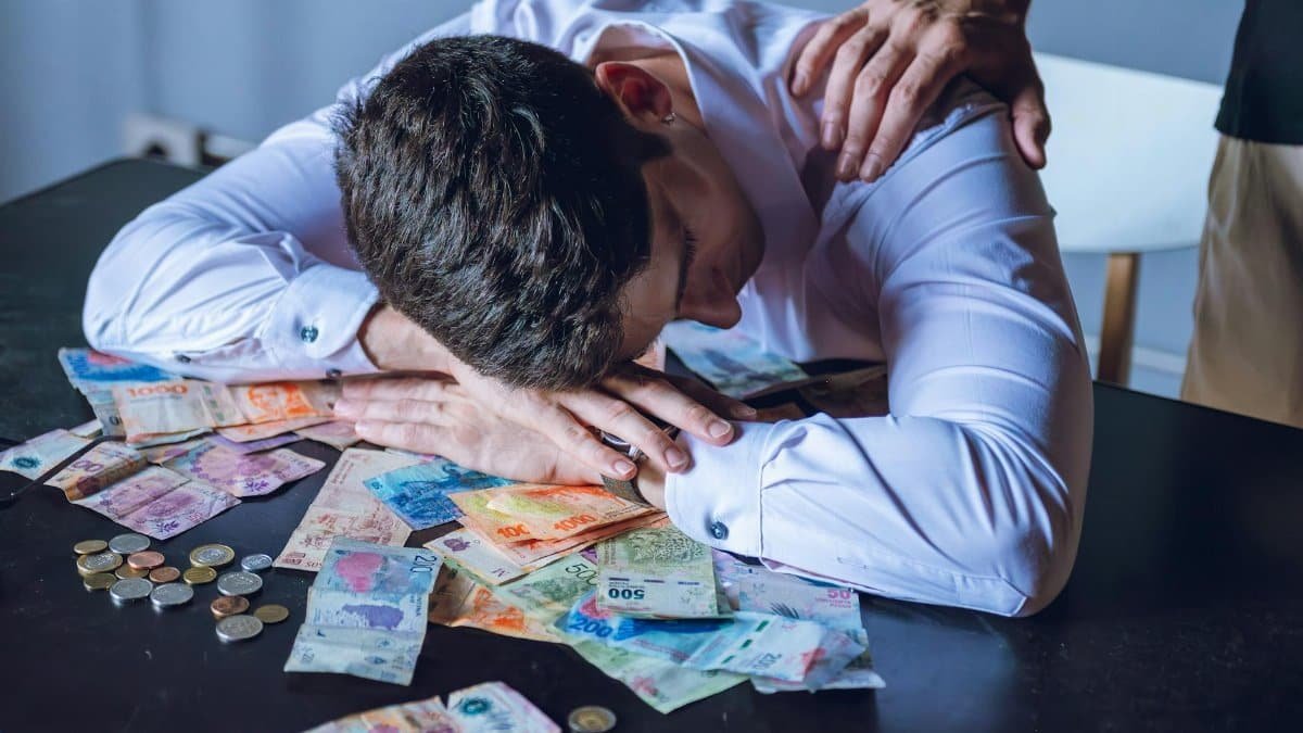 A man is overwhelmed with Argentine pesos, reflecting financial stress and support from another person.