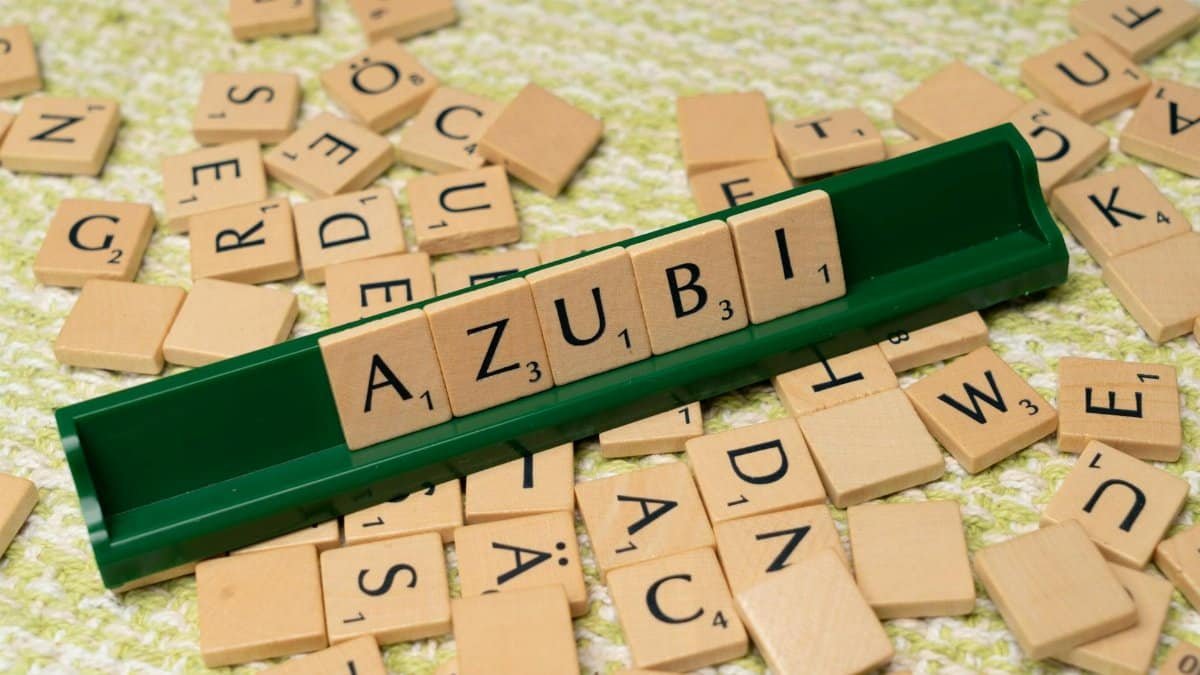 Close-up of wooden letter tiles forming the word 'Azubi' on a green rack with scattered tiles.