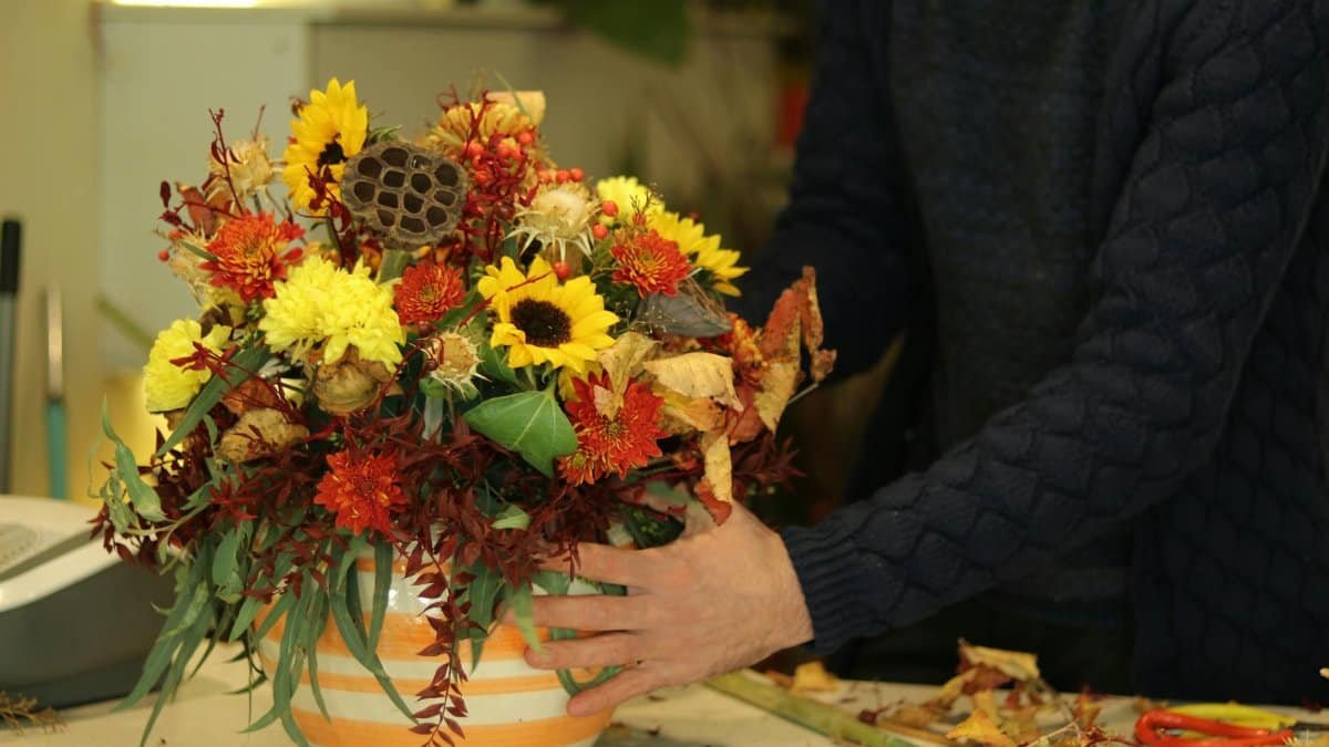 A colorful floral arrangement featuring sunflowers and autumn foliage in a decorated vase.