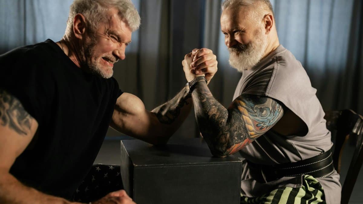 Two senior men engaged in an intense arm wrestling match indoors.