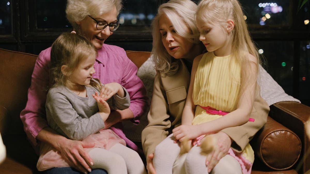 A warm family moment indoors with two grandmothers and two granddaughters sitting together on a sofa.