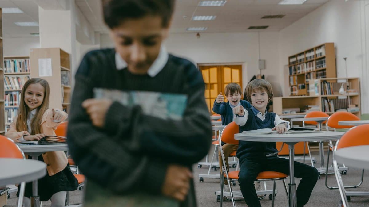 A group of children laughing and pointing at a sad classmate in a school library.