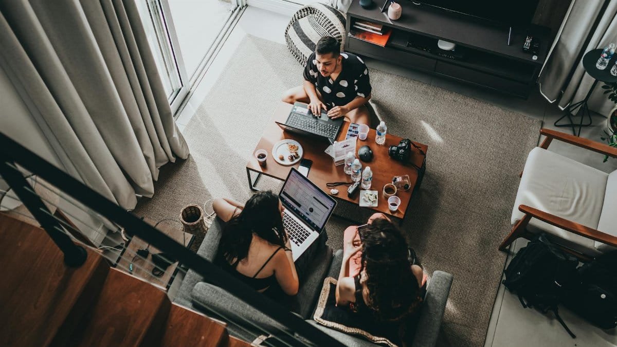 From above of young male and female remote workers sitting together around table with drinks and working on laptops