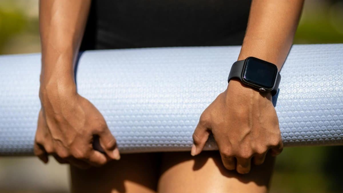 Close-up of hands holding a yoga mat, wearing a smartwatch, showcasing fitness lifestyle.