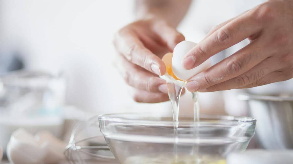 Hands carefully separating egg yolks and whites into a bowl, perfect for culinary content.