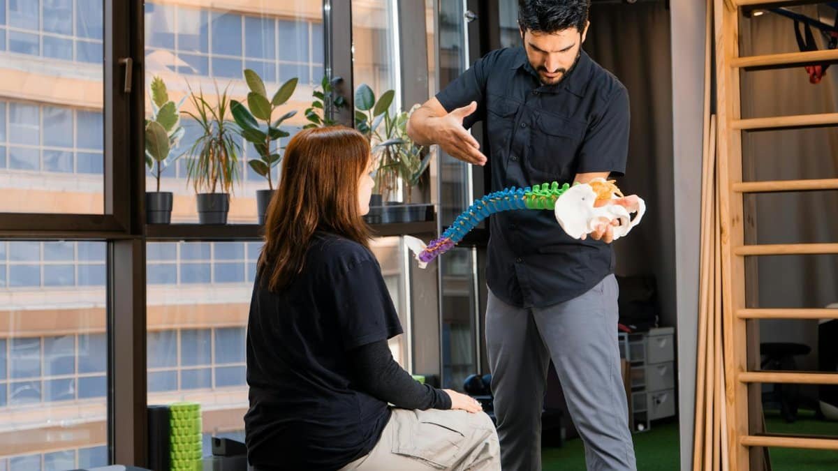 Chiropractor demonstrating spine anatomy to a patient during consultation indoors.