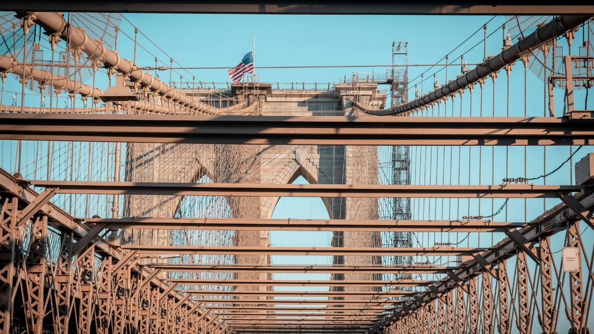 Iconic Brooklyn Bridge with American flag in clear daylight, showcasing its intricate architecture.